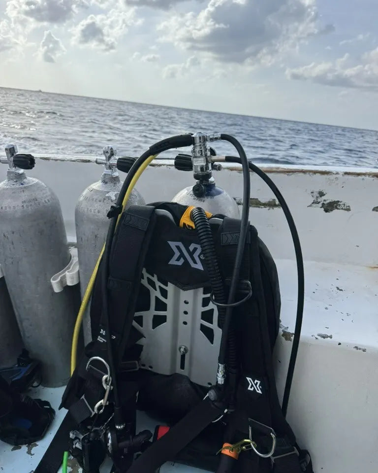 xDEEP backplate and wing on a dive tank on the deck of a dive boat, above the regulator on the valve, behind it the open sea
