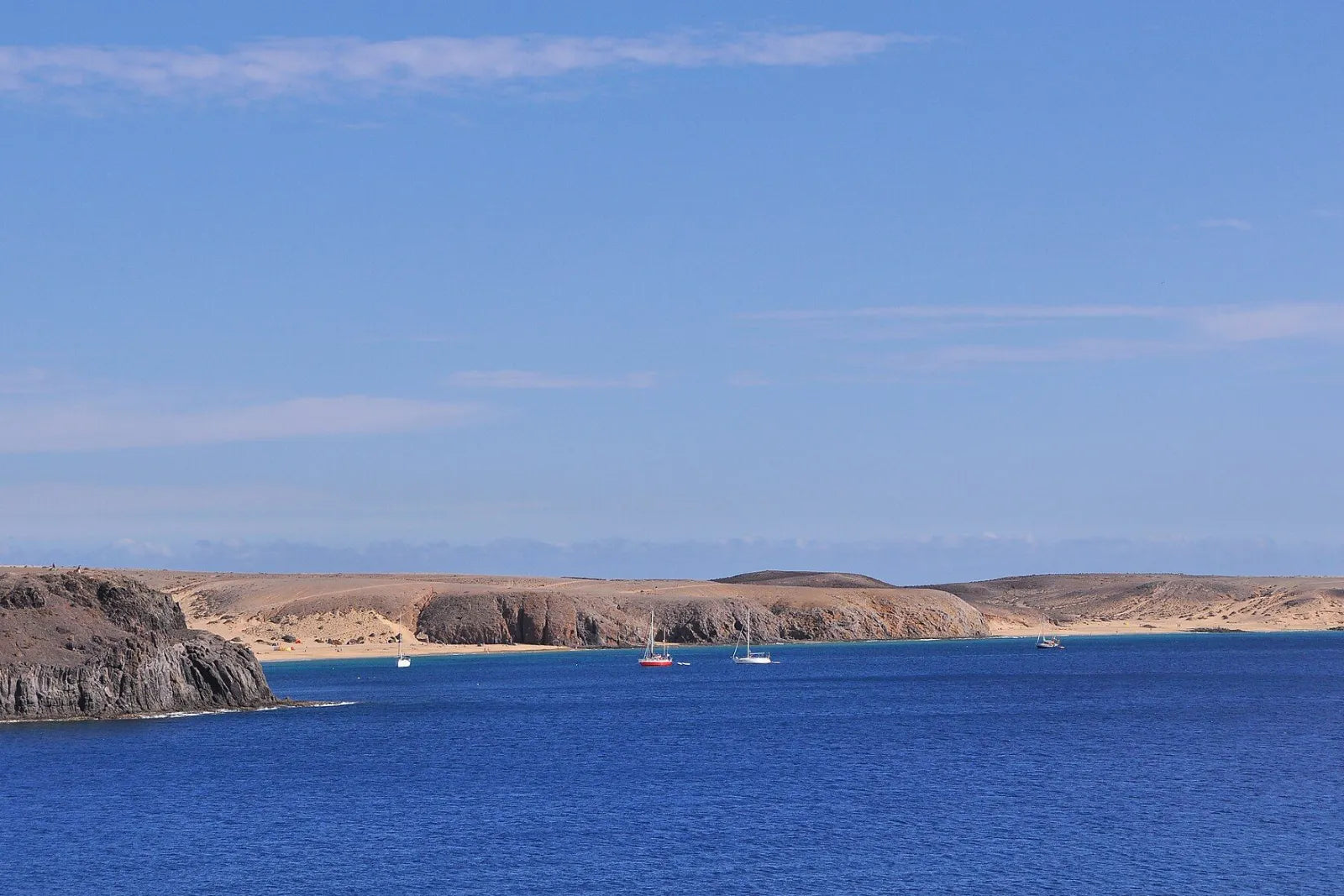 Baie d’un bleu profond avec des voiliers à l’ancre devant des falaises peu profondes couleur sable