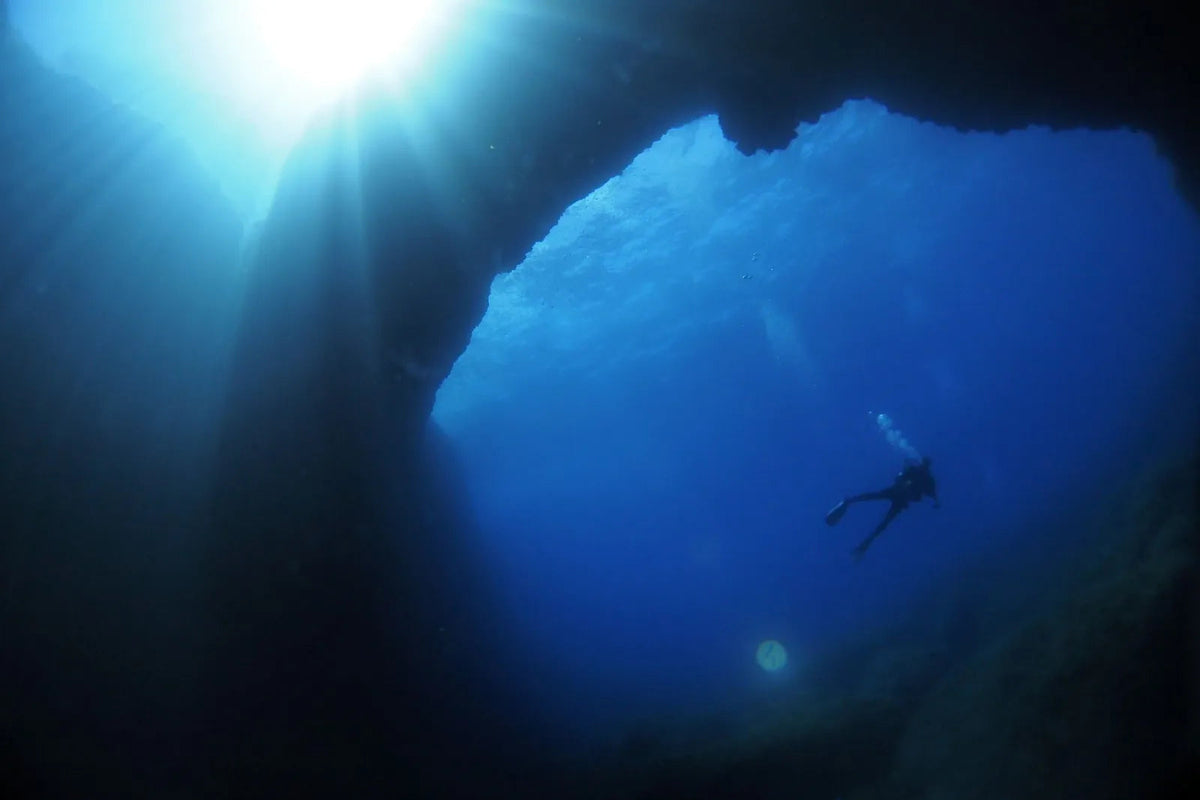 Blick aus dem Blue Hole nach oben, die Sonne steht über der Öffnung, ein Taucher schwebt im Blau