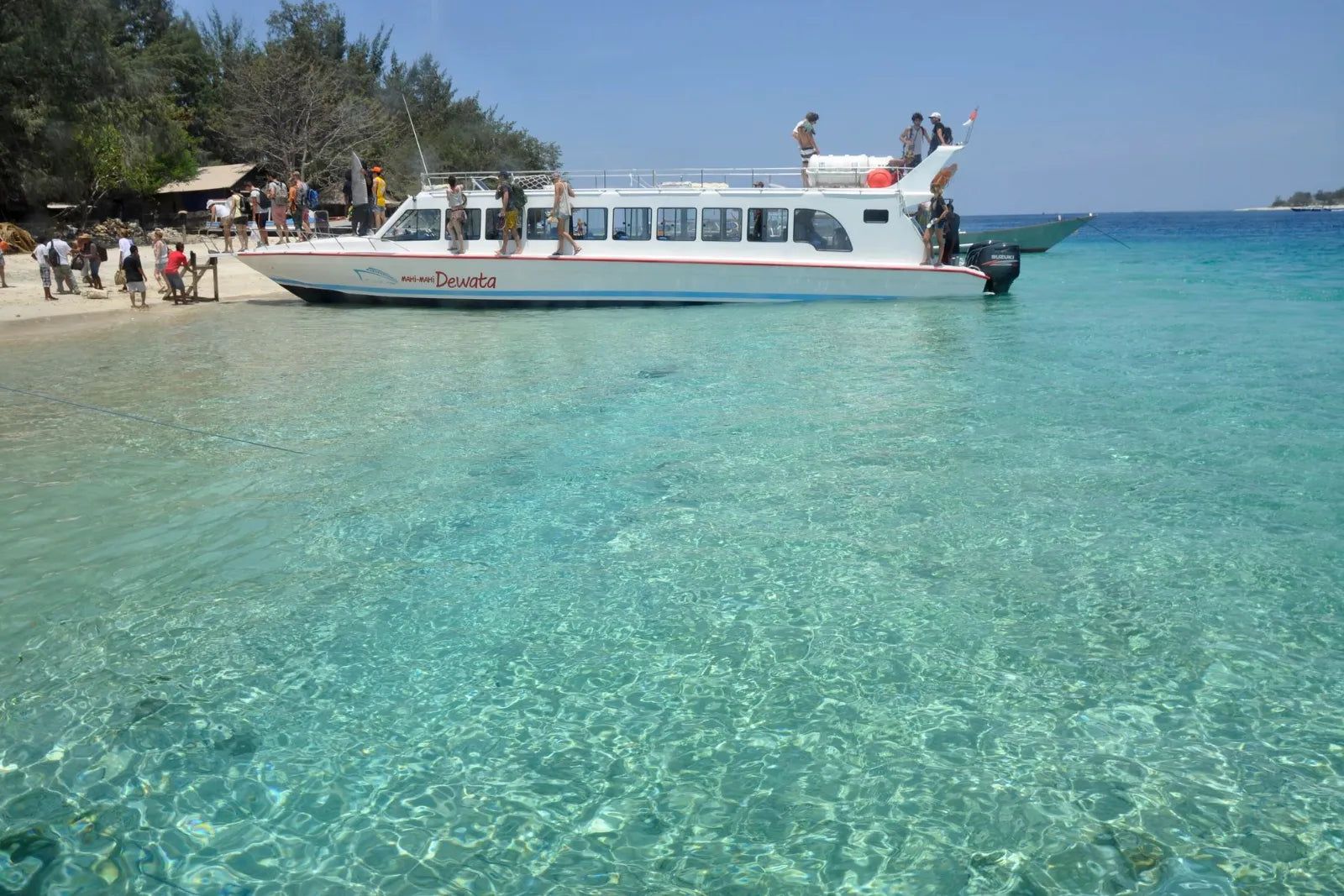 Bateau rapide blanc sur une plage de sable, devant une eau turquoise et claire sur un fond clair