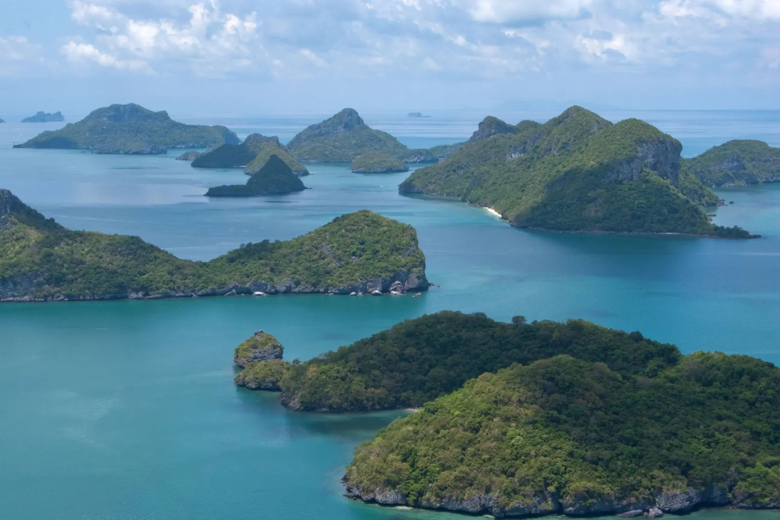 Many forested islands with steep rocky coasts in the turquoise sea, seen from above